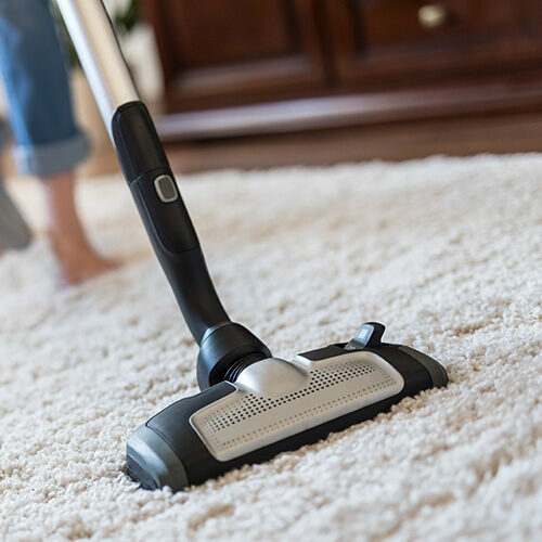 Woman cleaning area rug using vacuum cleaner | Howmar Carpet Inc